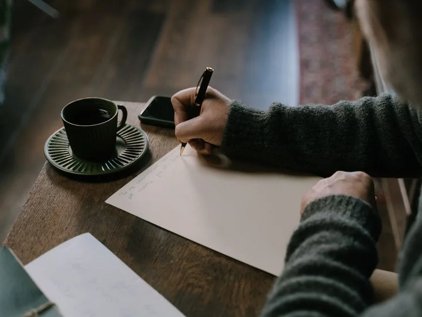 Mains qui écrivent dans un carnet près d’une tasse de café